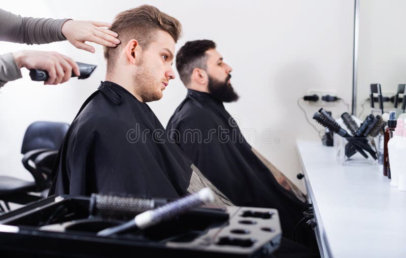 Jeunes clients faisant couper leurs cheveux par des coiffeurs