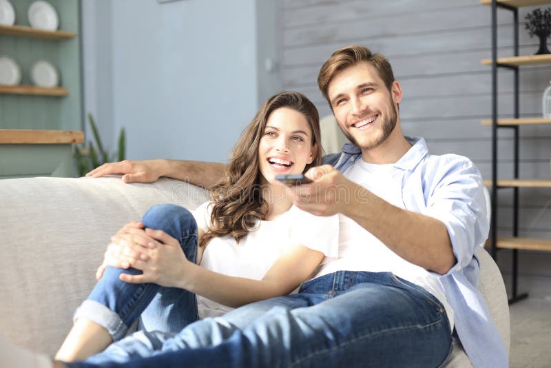 Jeunes couples affectueux sur le sofa ? la maison observant la TV et rire images libres de droits Jeunes couples affectueux sur le sofa ? la maison observant la TV et rire images libres de droits