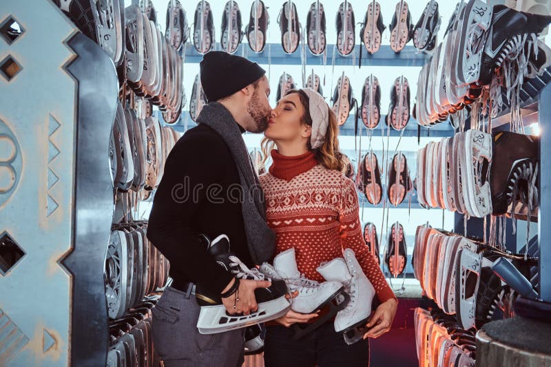 Jeunes couples dans l'amour, baiser tout en se tenant près du support avec beaucoup de paires de patins image stock Jeunes couples dans l'amour, baiser tout en se tenant près du support avec beaucoup de paires de patins image stock