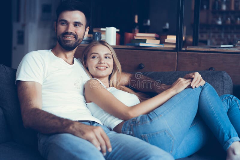 Jeunes couples de sourire détendant et regardant la TV à la maison photographie stock