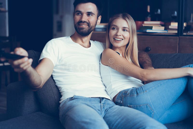 Jeunes couples de sourire détendant et regardant la TV à la maison photos libres de droits