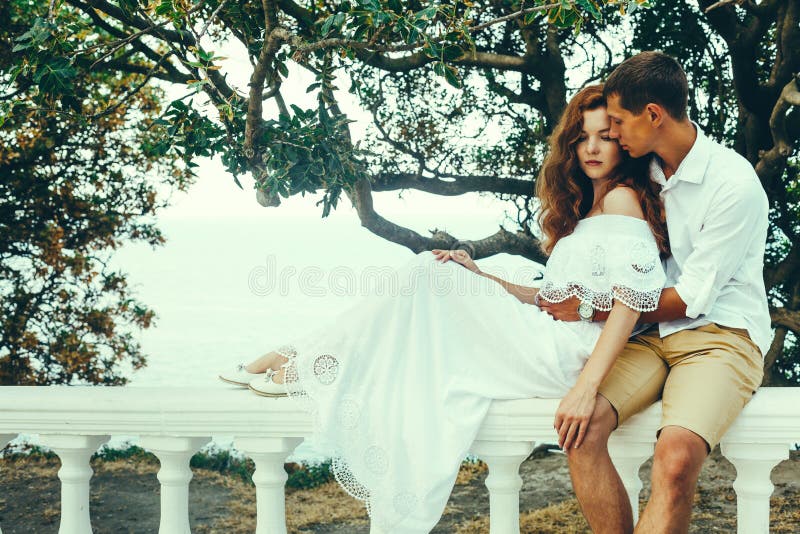 Jeunes couples des amants s'asseyant sur une balustrade, homme étreignant une femme Détendez le concept de mode de vie ensemble image stock Jeunes couples des amants s'asseyant sur une balustrade, homme étreignant une femme Détendez le concept de mode de vie ensemble image stock