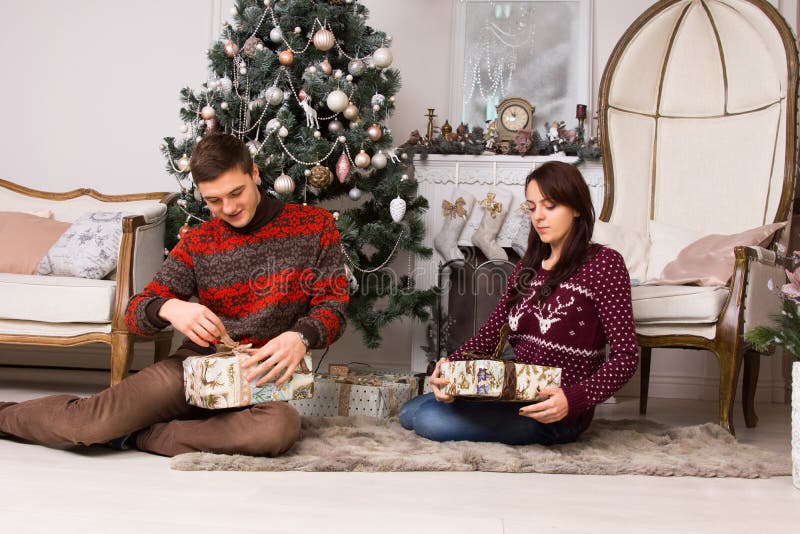 Jeunes couples déroulant leurs cadeaux de Noël photos stock Jeunes couples déroulant leurs cadeaux de Noël photos stock