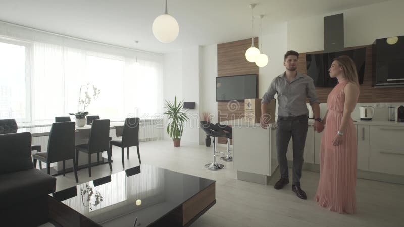 Jeunes couples enthousiastes heureux regardant autour de la conception à la mode moderne de cuisine intérieure se déplaçant en no banque de vidéos