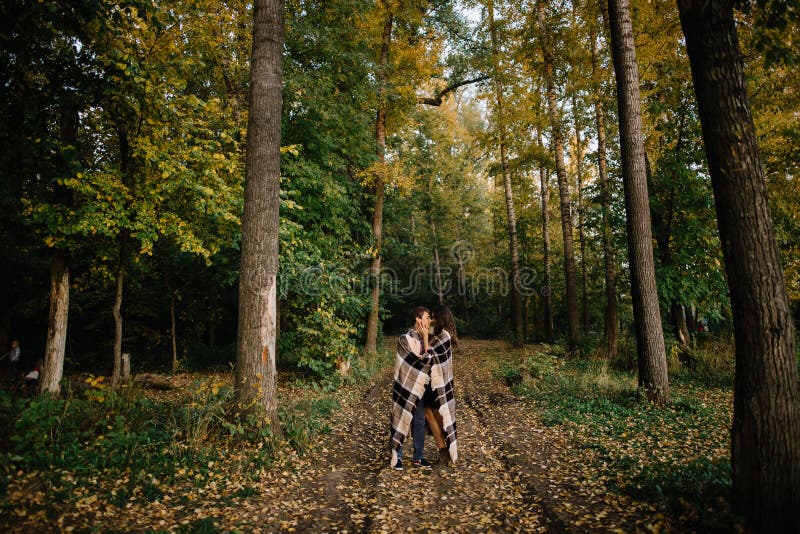 Jeunes couples enveloppés dans une couverture chaude dans la forêt d'automne photos libres de droits Jeunes couples enveloppés dans une couverture chaude dans la forêt d'automne photos libres de droits