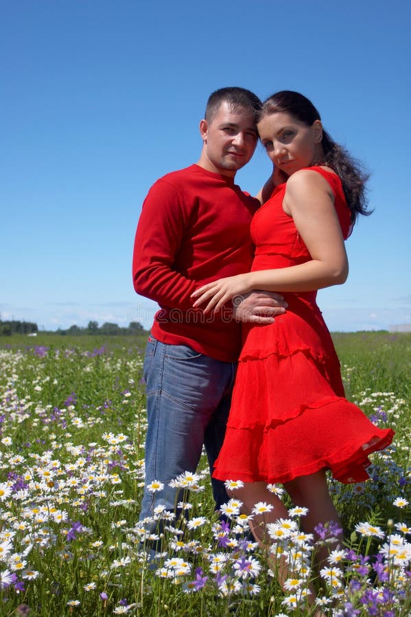 Young happy couple at the sunny day in a field with camomiles and handbells. Young happy couple at the sunny day in a field with camomiles and handbells