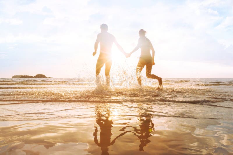 Jeunes couples heureux ayant l'amusement sur la plage au coucher du soleil, éclaboussure de l'eau