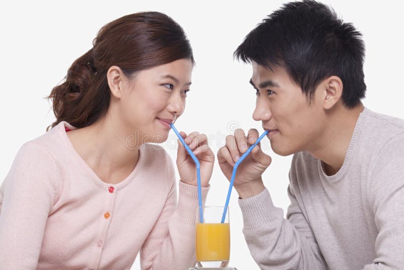 Jeunes couples heureux collant et partageant un verre de jus d'orange, tir de studio photographie stock Jeunes couples heureux collant et partageant un verre de jus d'orange, tir de studio photographie stock