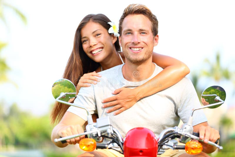 Happy young couple in love on scooter driving together. Multiracial couple having fun in the free outdoor. Smiling Caucasian men and Asian woman. Happy young couple in love on scooter driving together. Multiracial couple having fun in the free outdoor. Smiling Caucasian men and Asian woman.