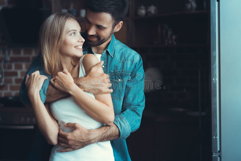 Jeunes couples heureux étreignant et regardant l'un l'autre à l'intérieur d'une nouvelle cuisine, bonheur dans une nouvelle maiso image libre de droits