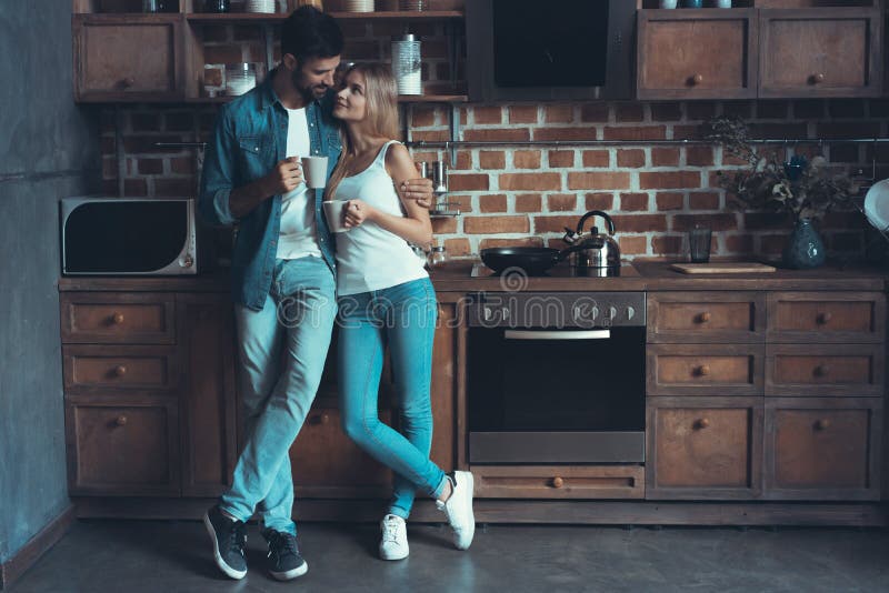 Jeunes couples heureux étreignant et regardant l'un l'autre à l'intérieur d'une nouvelle cuisine, bonheur dans une nouvelle maiso photo stock
