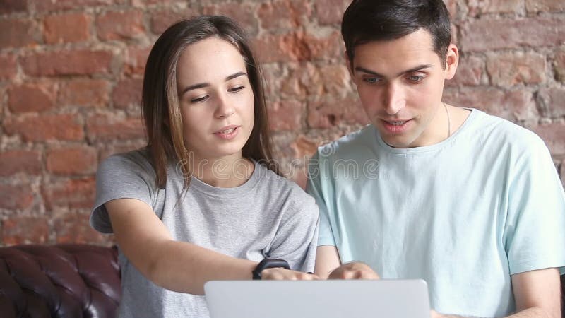Jeunes couples occasionnels utilisant l'ordinateur portable, choisissant des marchandises dans la boutique en ligne