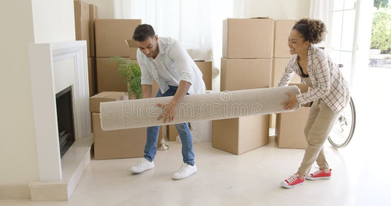 Jeunes couples portant une couverture roulée dans une maison photographie stock Jeunes couples portant une couverture roulée dans une maison photographie stock