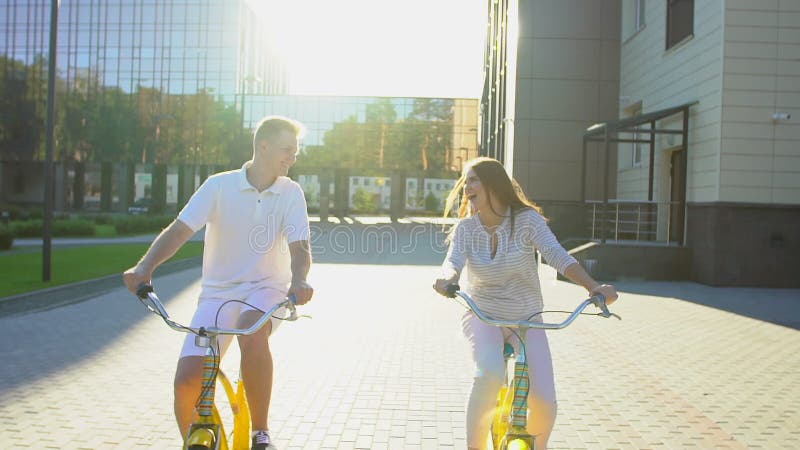 Jeunes couples romantiques heureux faisant un cycle heureusement ensemble par une rue ensoleillée dans l'été dehors Type et fille banque de vidéos