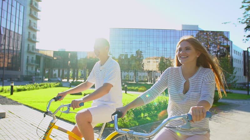 Jeunes couples romantiques heureux faisant un cycle heureusement ensemble par une rue ensoleillée dans l'été dehors Type et fille banque de vidéos