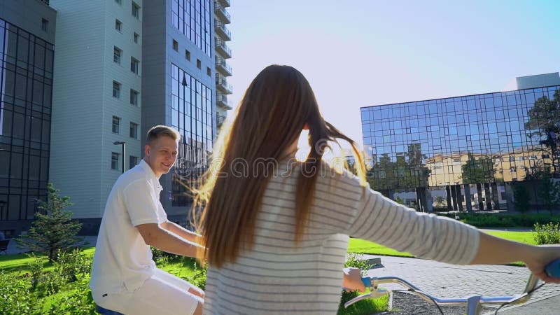 Jeunes couples romantiques heureux faisant un cycle heureusement ensemble par une rue ensoleillée dans l'été dehors Type et fille clips vidéos