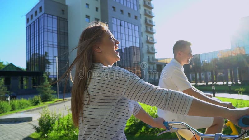 Jeunes couples romantiques heureux faisant un cycle heureusement ensemble par une rue ensoleillée dans l'été dehors Type et fille banque de vidéos