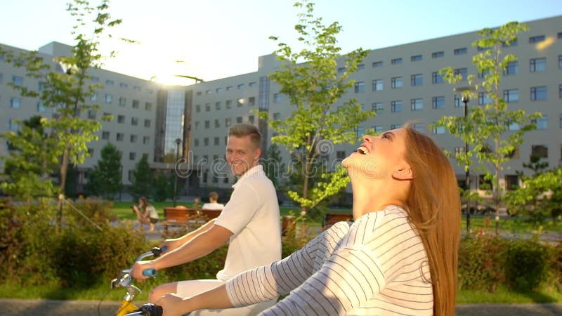 Jeunes couples romantiques heureux faisant un cycle heureusement ensemble par une rue ensoleillée dans l'été dehors Type et fille banque de vidéos