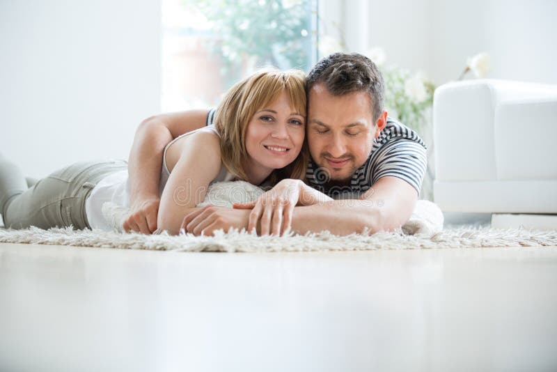Jeunes couples se situant dans le salon sur le tapis, embrassant photographie stock Jeunes couples se situant dans le salon sur le tapis, embrassant photographie stock