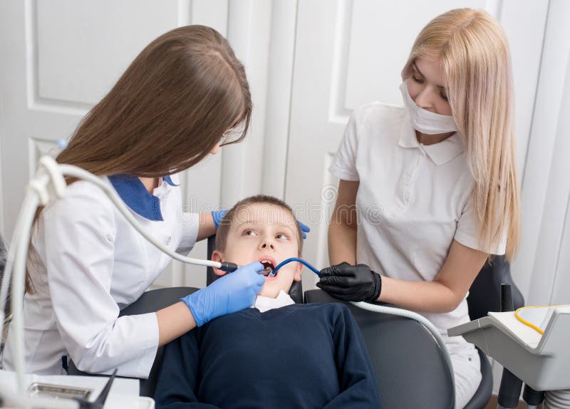 Jeunes dentistes féminins examinant et travaillant au patient de garçon images stock Jeunes dentistes féminins examinant et travaillant au patient de garçon images stock