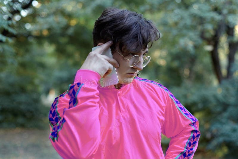 Jeunes entretiens caucasiens beaux d'homme au téléphone portable se tenant en parc Verres d'or ronds, chemise lilas lumineuse, to images libres de droits Jeunes entretiens caucasiens beaux d'homme au téléphone portable se tenant en parc Verres d'or ronds, chemise lilas lumineuse, to images libres de droits