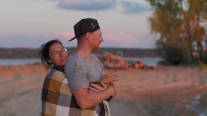 Jeunes femme et homme de couple sur une plage de sable au coucher du soleil dans une couverture de écossais. Les amateurs de march clips vidéos