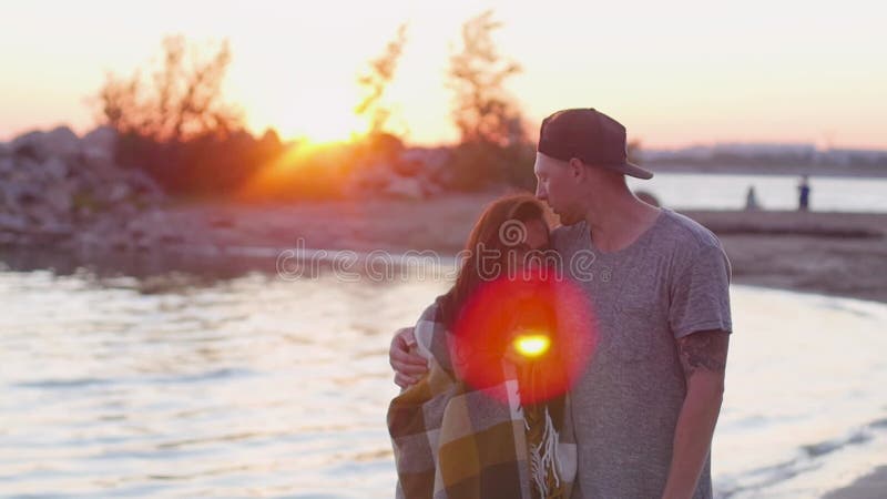 Jeunes femme et homme de couple sur une plage de sable au coucher du soleil dans une couverture de écossais. Les amateurs de march banque de vidéos