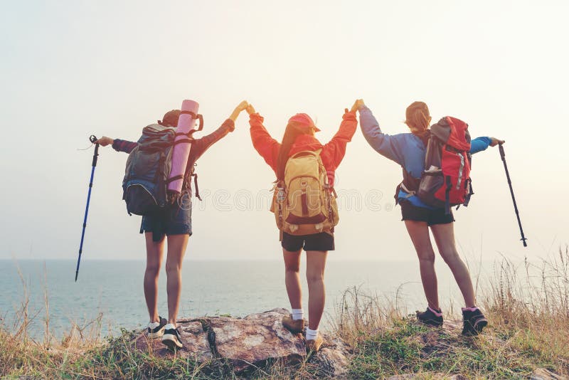 Group friend team asian young women of hikers walking adventure with backpack on a mountain at sunset. Traveler life going trip camping outdoors. Travel and Vacations Concept. Group friend team asian young women of hikers walking adventure with backpack on a mountain at sunset. Traveler life going trip camping outdoors. Travel and Vacations Concept