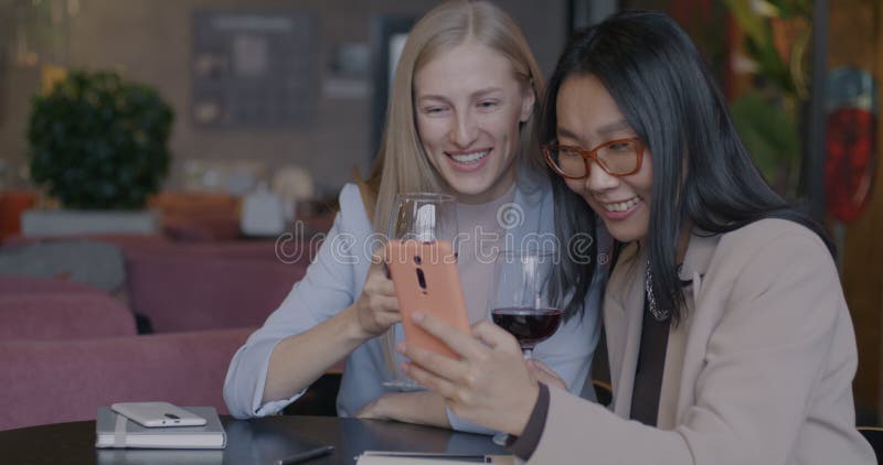 Jeunes femmes d'affaires joyeuses utilisant smartphone et rire boire du vin rouge au café banque de vidéos