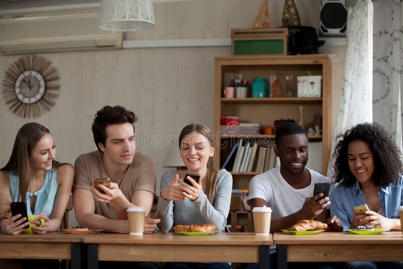 Jeunes femmes et hommes divers de sourire à l'aide des smartphones en café photo stock Jeunes femmes et hommes divers de sourire à l'aide des smartphones en café photo stock