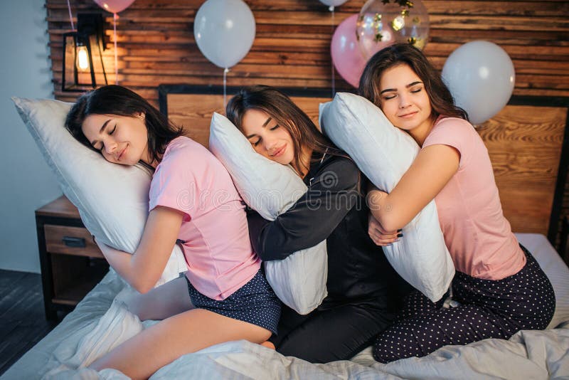 Jeunes femmes somnolentes s'asseyant sur le lit dans la chambre Leur tête se trouvant sur des oreillers qu'ils ont dans des mains photographie stock libre de droits Jeunes femmes somnolentes s'asseyant sur le lit dans la chambre Leur tête se trouvant sur des oreillers qu'ils ont dans des mains photographie stock libre de droits