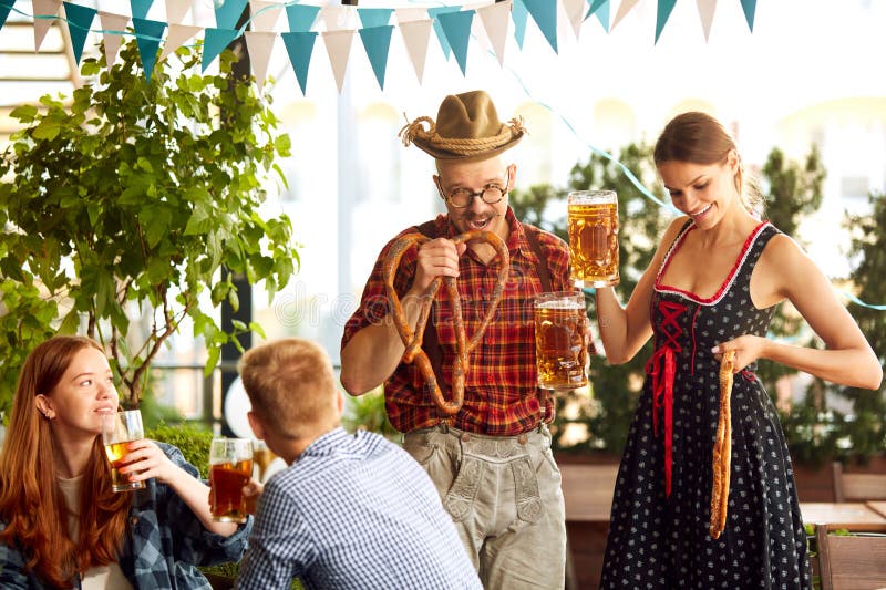 Young stylish people in bavarian clothes drinking beer and eating lager beer at pub. Friends meeting for celebration. Concept of oktoberfest, traditional taste, friendship, leisure time, enjoyment. Young stylish people in bavarian clothes drinking beer and eating lager beer at pub. Friends meeting for celebration. Concept of oktoberfest, traditional taste, friendship, leisure time, enjoyment