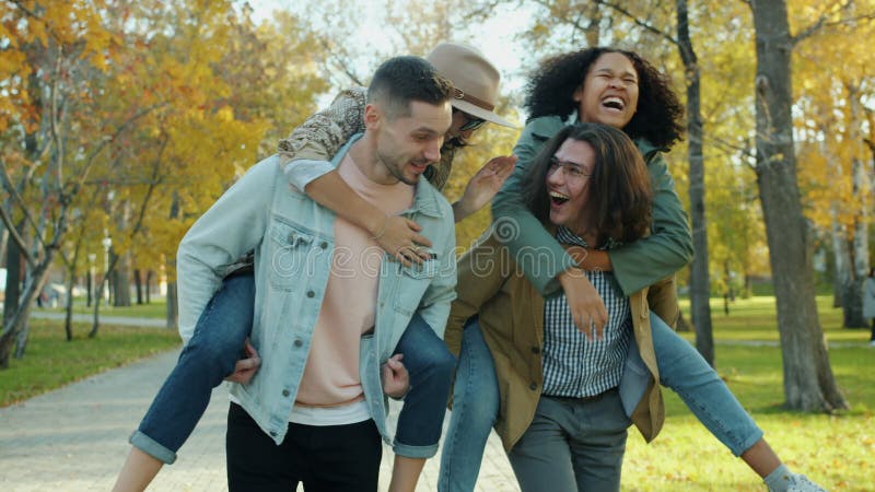 Jeunes hommes joyeux donnant sur le dos au tour des femmes heureuses s'amusant dans le parc clips vidéos