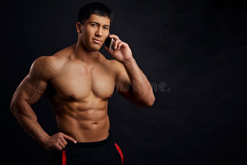 Jeunes hommes sans chemise asiatiques beaux posant et téléphone portable de holdiong image stock Jeunes hommes sans chemise asiatiques beaux posant et téléphone portable de holdiong image stock