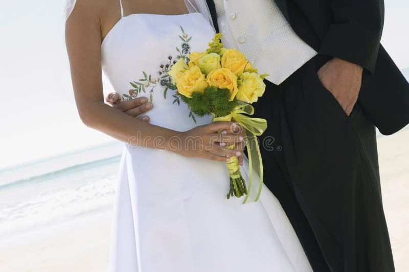 Jeunes mariés avec le bouquet sur la plage (plan rapproché) images stock Jeunes mariés avec le bouquet sur la plage (plan rapproché) images stock