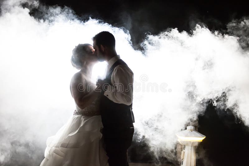 Jeunes mariés embrassant en brouillard la nuit image stock