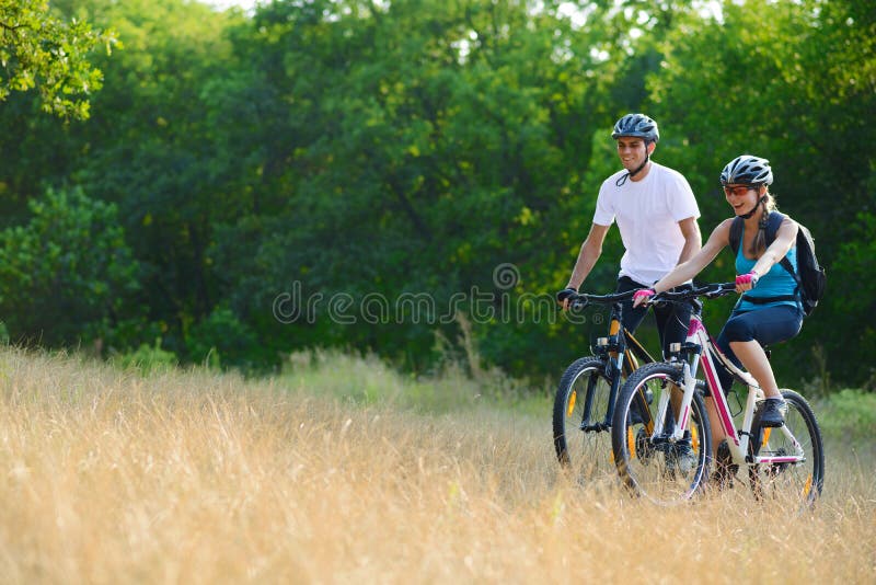 Jeunes vélos de montagne heureux d'équitation de couples extérieurs images stock Jeunes vélos de montagne heureux d'équitation de couples extérieurs images stock