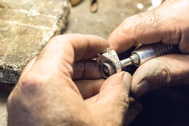 Male jeweler polishing a silver ring with a slotted mandrel for sandpaper, mounted on a flex shaft. Male jeweler polishing a silver ring with a slotted mandrel for sandpaper, mounted on a flex shaft.