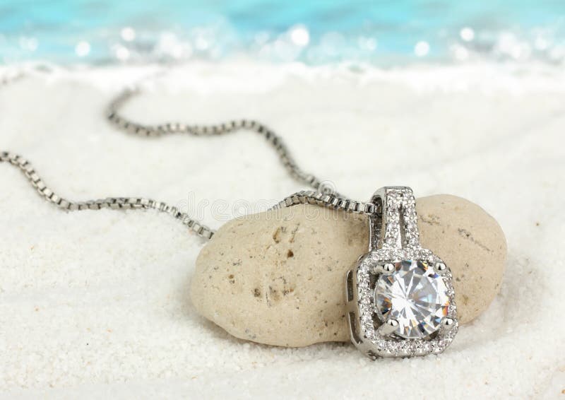 Jewelry pendant with big diamond on sand beach as background