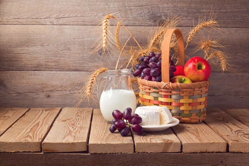 Jewish holiday Shavuot celebration. Basket with fruits and milk over wooden background