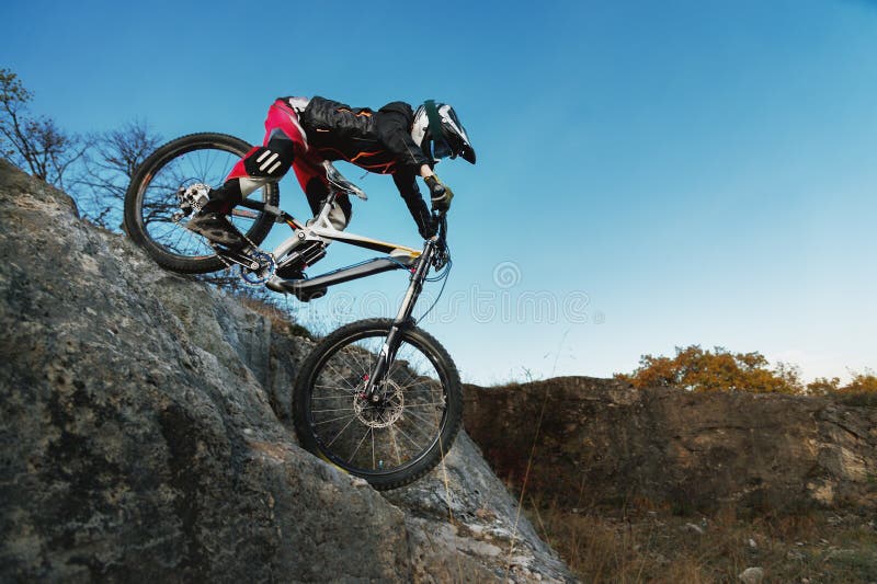 Jinete joven en la bici del mtb que baja de un acantilado contra un cielo azul foto de archivo libre de regalías Jinete joven en la bici del mtb que baja de un acantilado contra un cielo azul foto de archivo libre de regalías