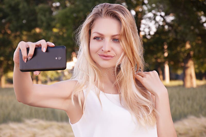 Jjunges schönes Mädchen, das sich im warmen Sommer im Freien mit Mobiltelefon selbst macht stockfoto Jjunges schönes Mädchen, das sich im warmen Sommer im Freien mit Mobiltelefon selbst macht stockfoto