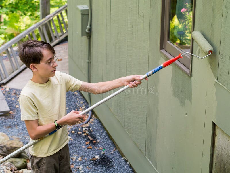 A teenage boy uses a paint roller to apply paint to the side of a house as a summer job. A teenage boy uses a paint roller to apply paint to the side of a house as a summer job.