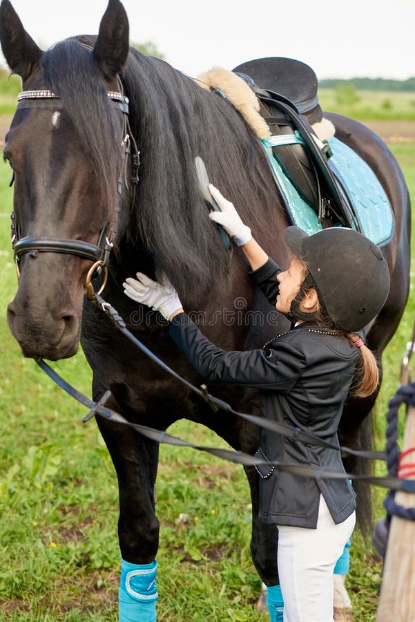 Jockey μικρών κοριτσιών παρευρίσκεται και βουρτσίζοντας το άλογό της στοκ εικόνες Jockey μικρών κοριτσιών παρευρίσκεται και βουρτσίζοντας το άλογό της στοκ εικόνες