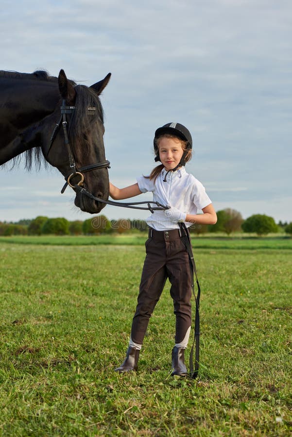 Jockey μικρών κοριτσιών που επικοινωνεί με το μαύρο άλογό της στην επαγγελματική εξάρτηση στοκ φωτογραφία Jockey μικρών κοριτσιών που επικοινωνεί με το μαύρο άλογό της στην επαγγελματική εξάρτηση στοκ φωτογραφία