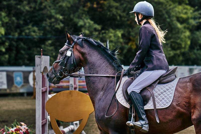 Jockeyn f? r den unga kvinnan i vitsvartkl? nningen och svartk? ngor, tagande s? rar i rid- konkurrenser royaltyfria foton