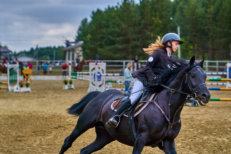 Jockeyn för den unga kvinnan i vitsvartklänningen och svartkängor, tagande särar i rid- konkurrenser royaltyfri fotografi