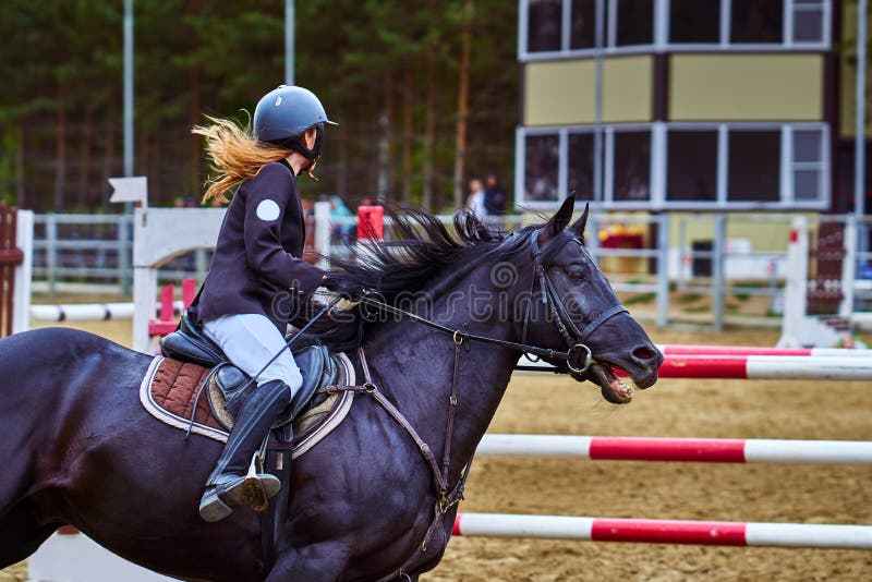 Jockeyn för den unga kvinnan i vitsvartklänningen och svartkängor, tagande särar i rid- konkurrenser arkivbilder