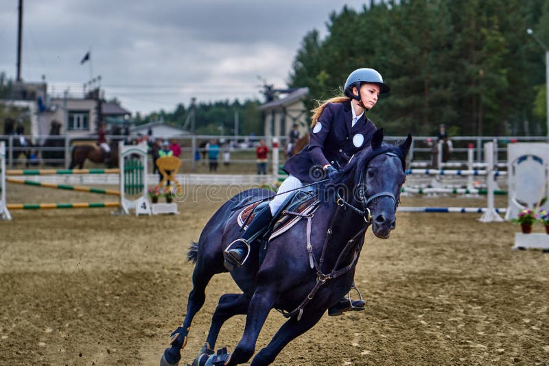 Jockeyn för den unga kvinnan i vitsvartklänningen och svartkängor, tagande särar i rid- konkurrenser arkivfoton