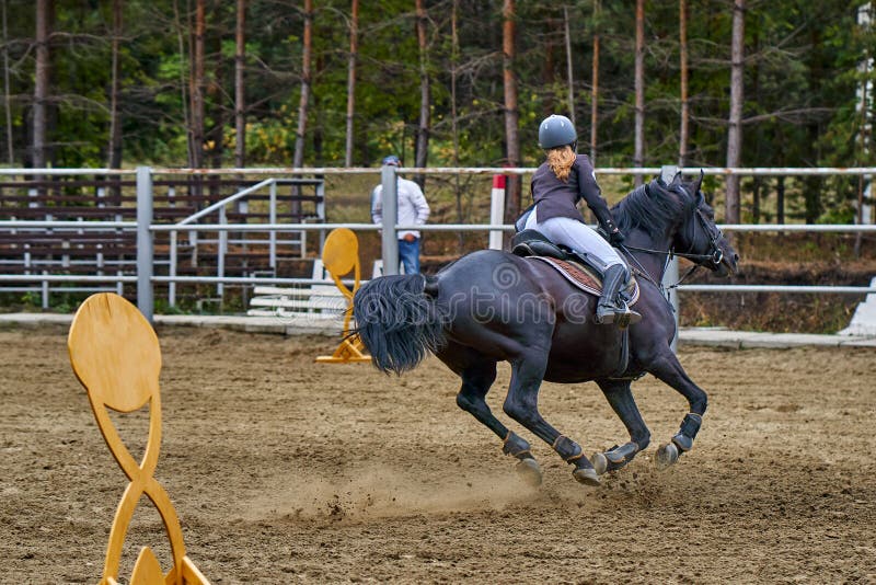 Jockeyn för den unga kvinnan i vitsvartklänningen och svartkängor, tagande särar i rid- konkurrenser arkivfoto